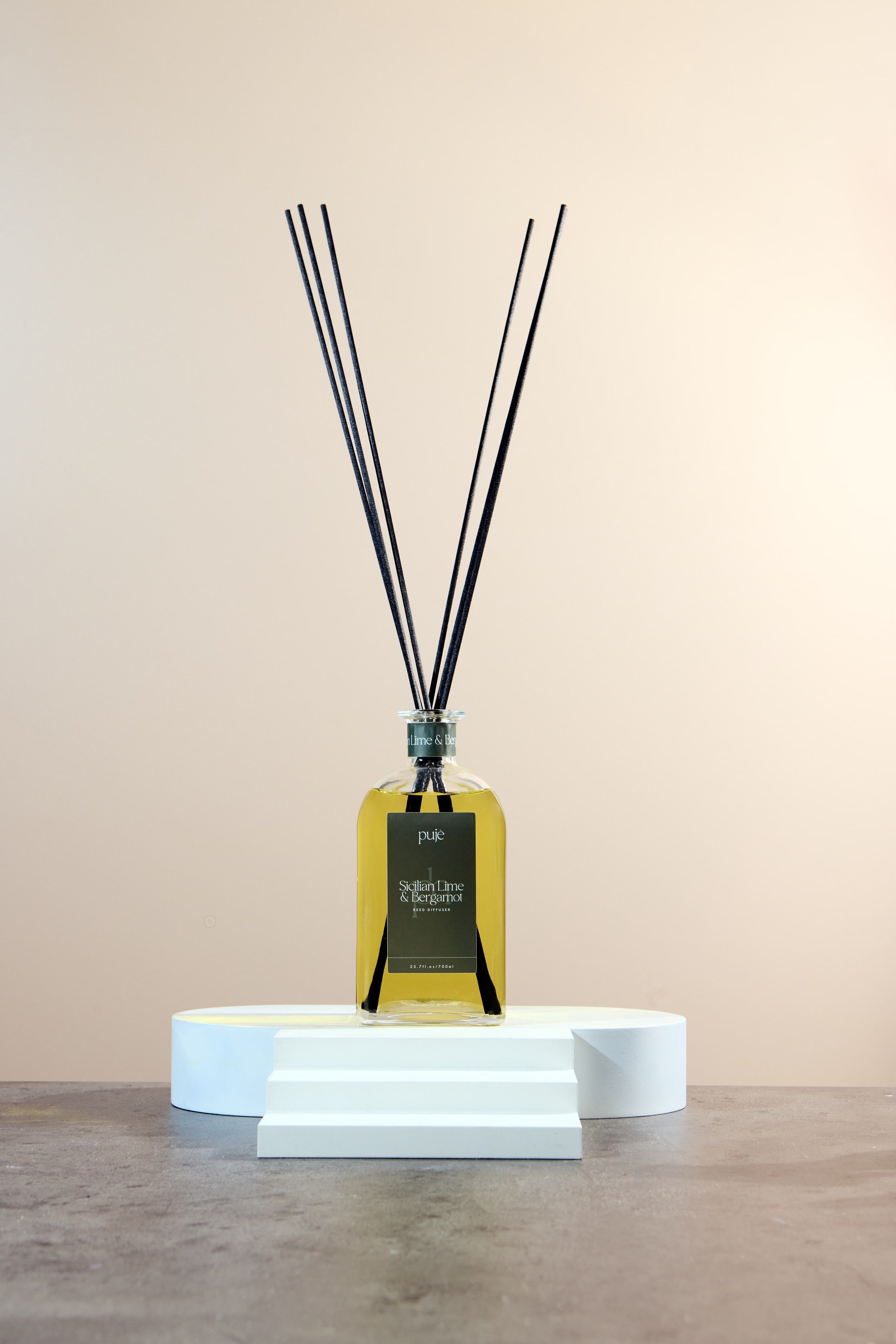 A glass bottle diffuser with black reeds and a green label that reads