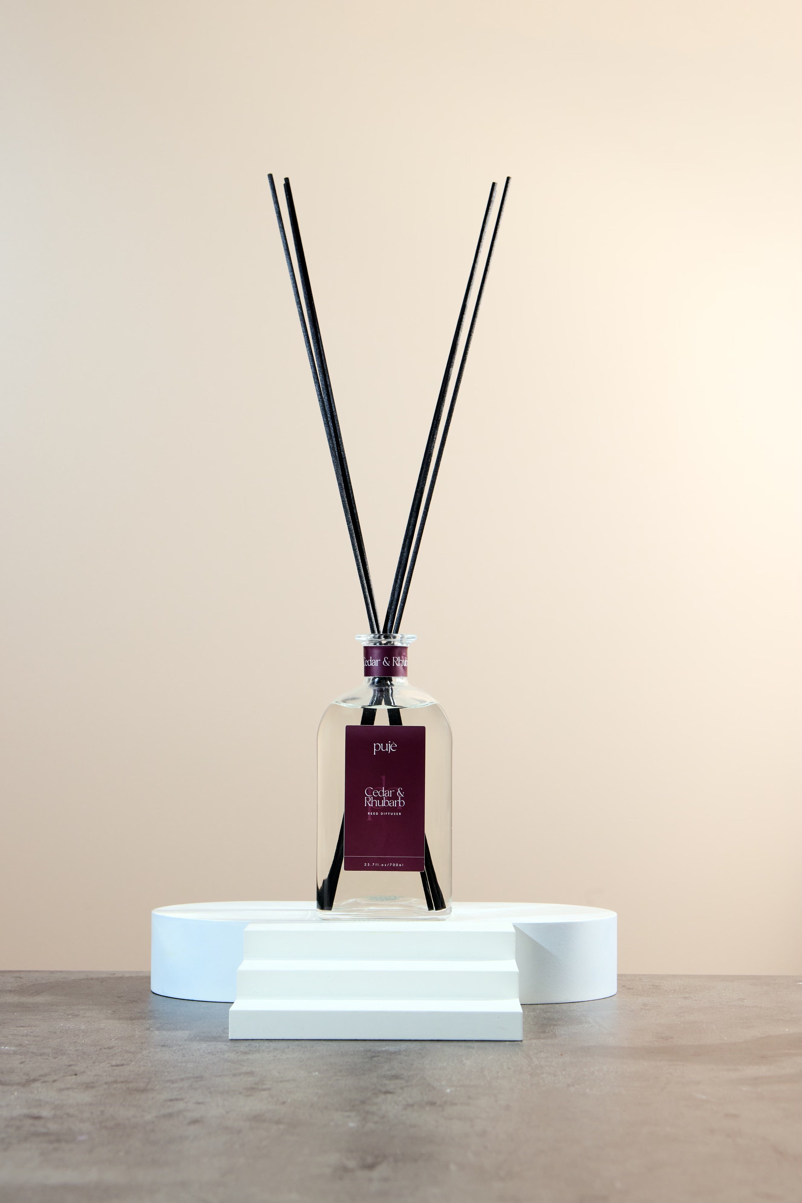 A glass bottle diffuser with black reeds and a burgundy label that reads