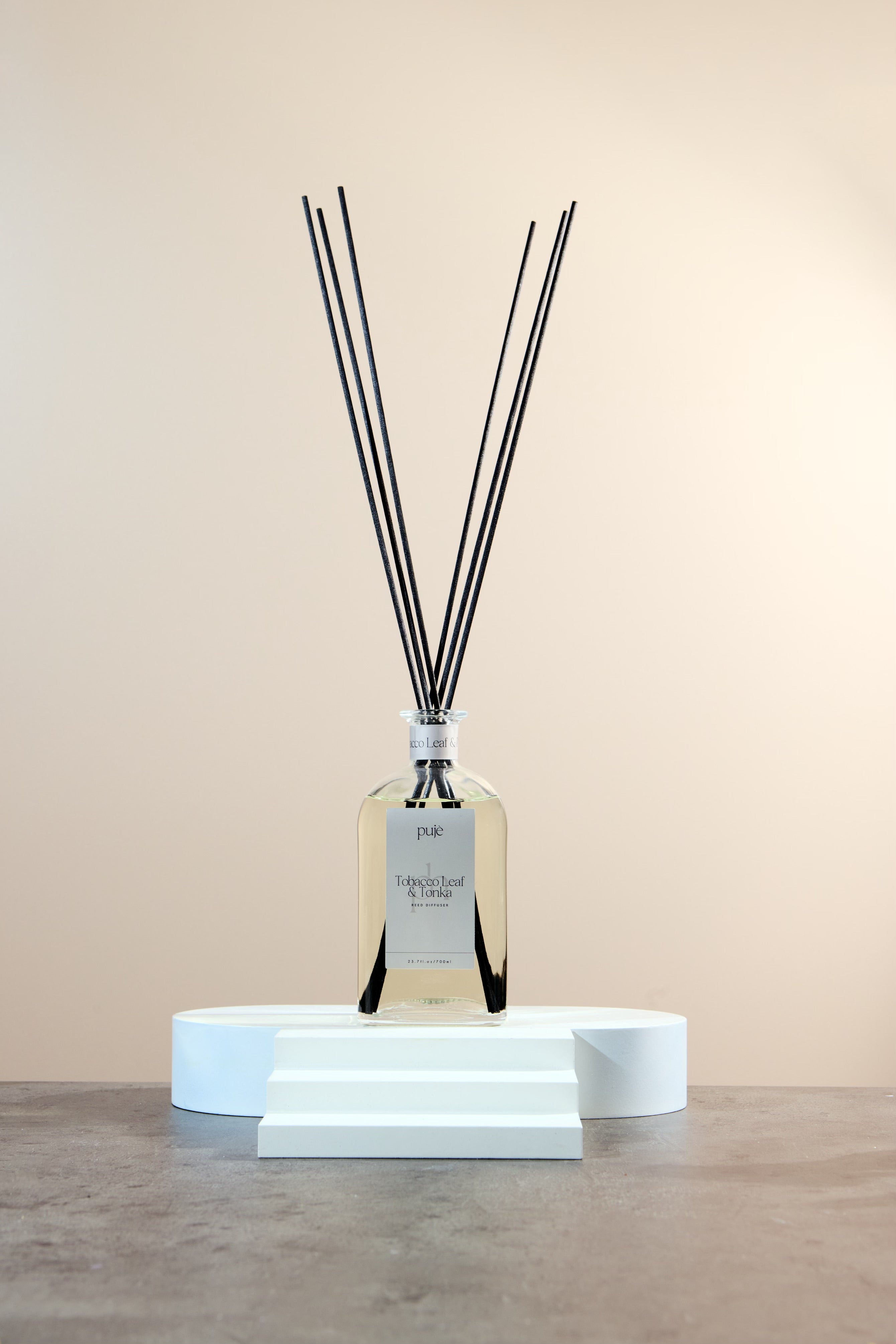 A glass bottle diffuser with black reeds and a silver nude label that reads 