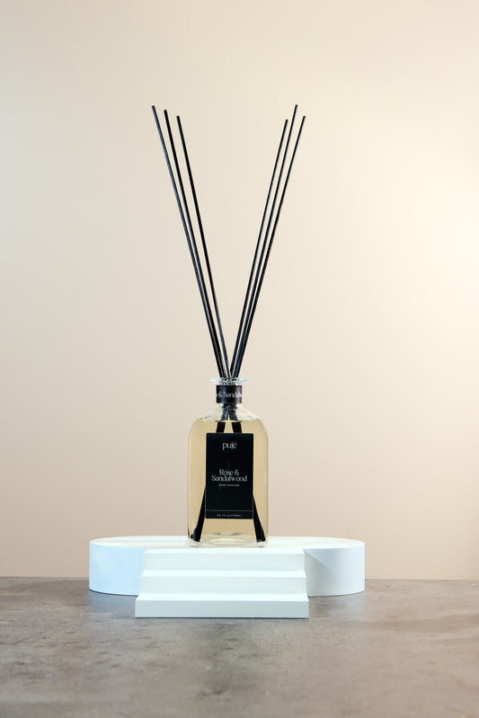 A glass bottle diffuser with black reeds and a black label that reads "Rose & Sandalwood Scented.